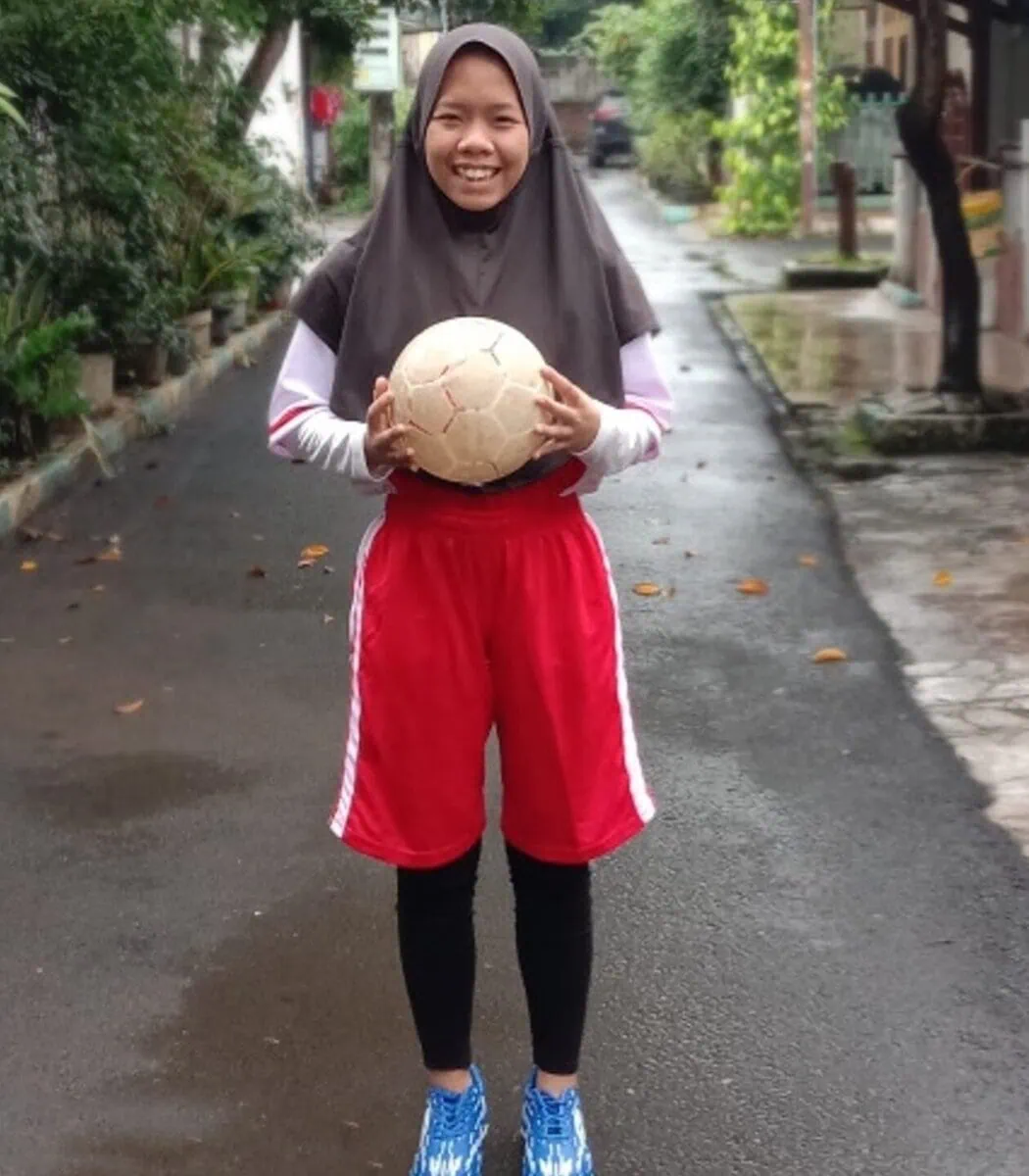 Foto remaja perempuan membawa bola sepak di sebuah gang pemukiman