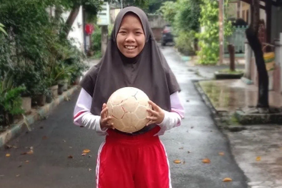 Foto remaja perempuan membawa bola sepak di sebuah gang pemukiman